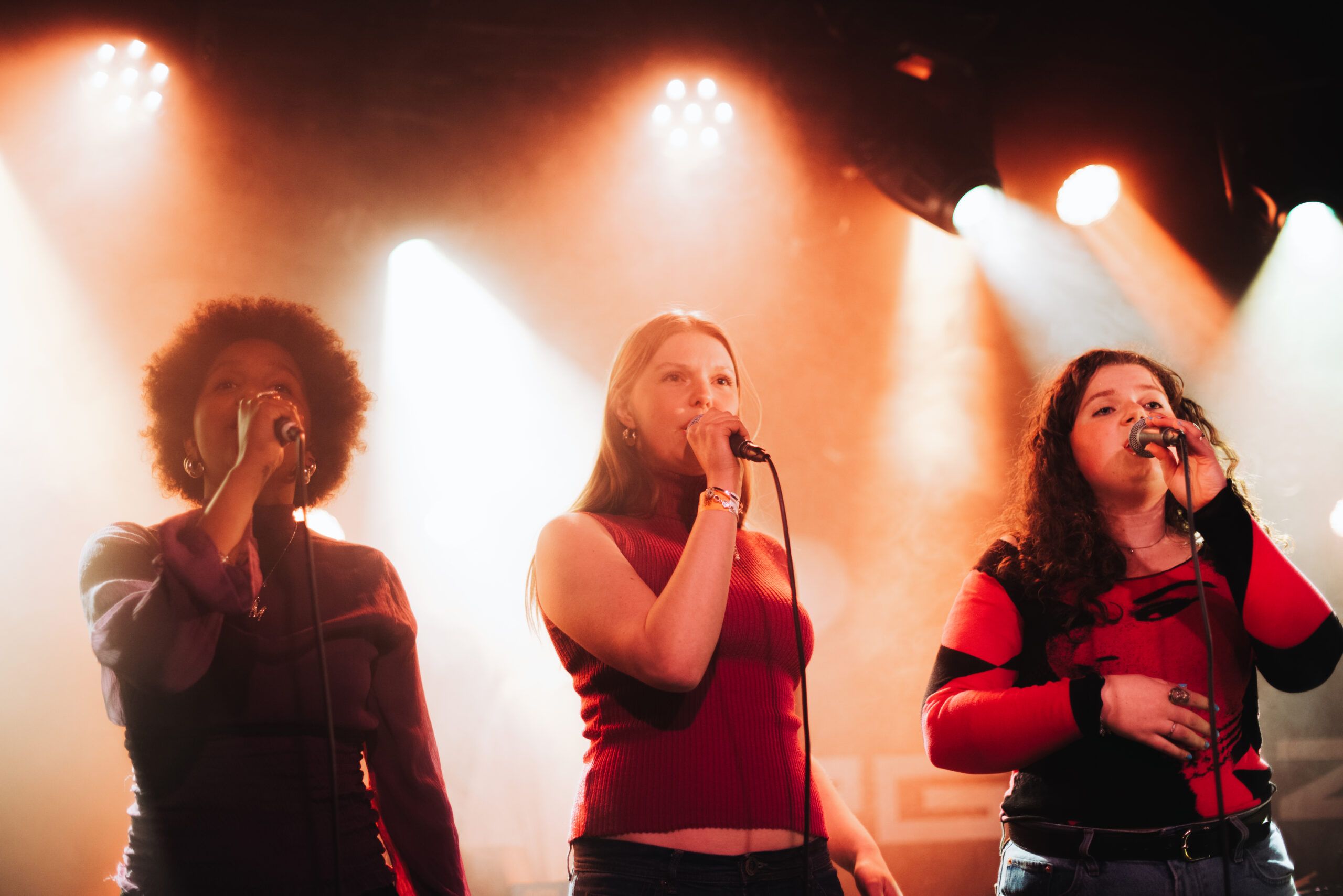 Tre jenter synger i rødt scenelys