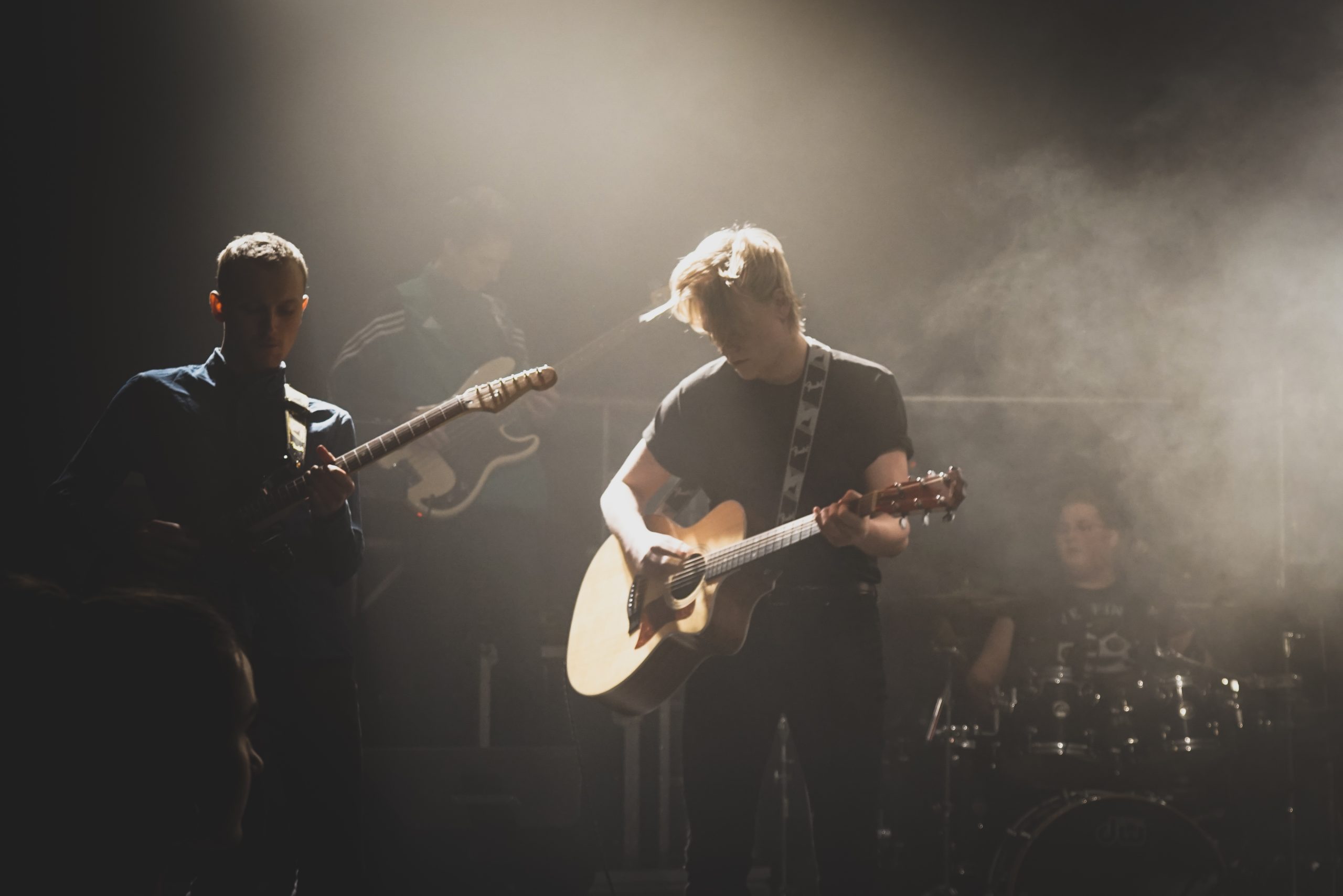 To gitarister og en trommeslager på røyklagt scene