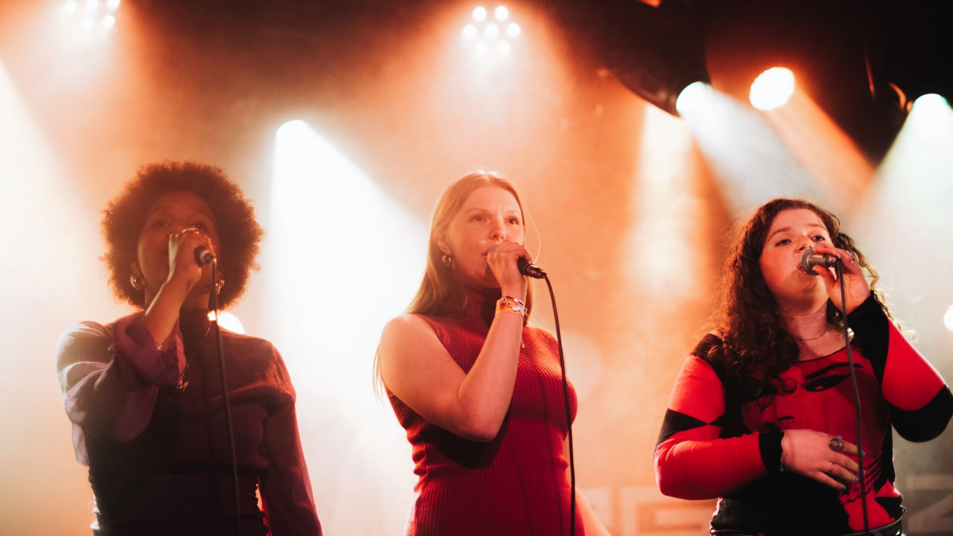 Tre jenter synger i rødt scenelys
